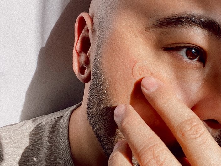 person touching pimple patch on face