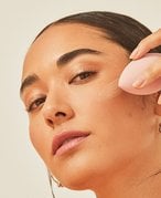 Picture of a model blending in foundation with a pink makeup sponge