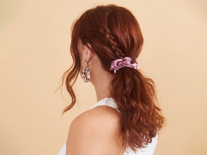 Picture of the back of a person’s head, with dyed red hair in a ponytail and a pink scrunchie, on a neutral-colored background