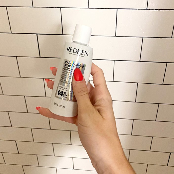 A person with red polished fingernails holding the Redken Acidic Bonding Concentrate Intensive Treatment.