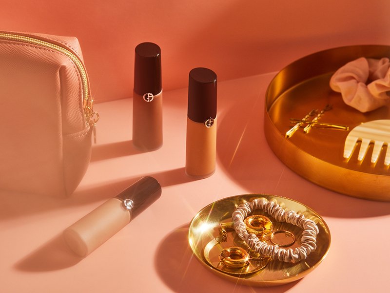 Countertop with several bottles of the Giorgio Armani Beauty Luminous Silk Concealer, a makeup bag, and trays with a silk scrunchie and jewelry 