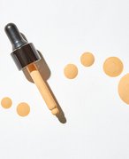 Image of foundation dropper and drops of foundation on white background