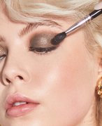 Close-up picture of a model applying a dark, glittery eyeshadow to their eyelid