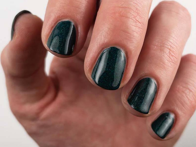 Close-up picture of a model's nails painted a shimmery dark green color
