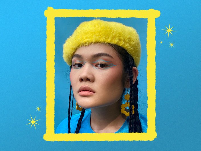 person wearing a yellow hat and blue and orange eye makeup against a blue background