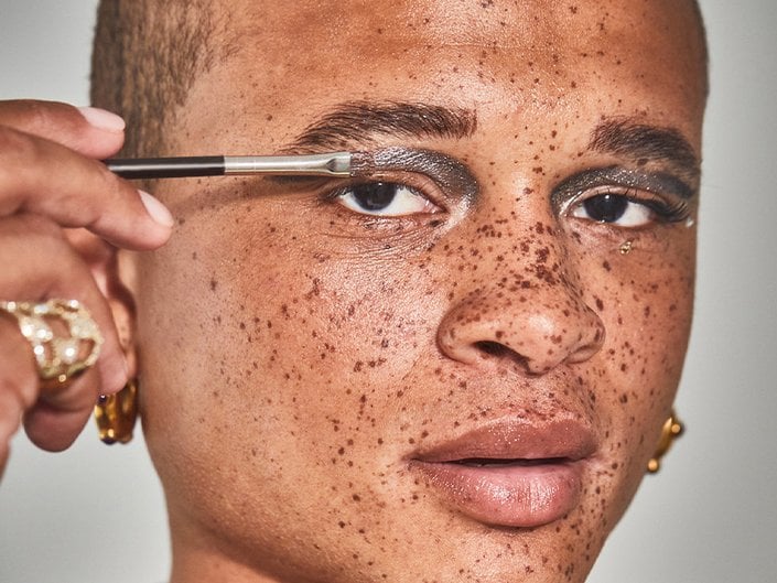 person applying metallic silver eyeshadow to their eyelid with a brush