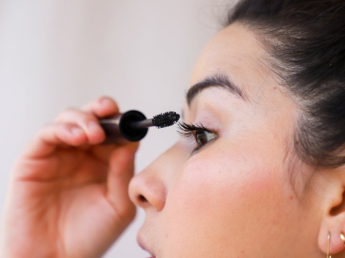 Close-up of person with dark hair in profile applying mascara to their eyelashes