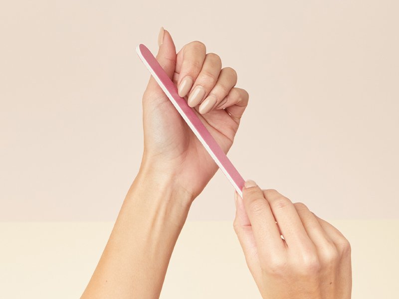 Picture of a person filing their nails on a cream-colored background
