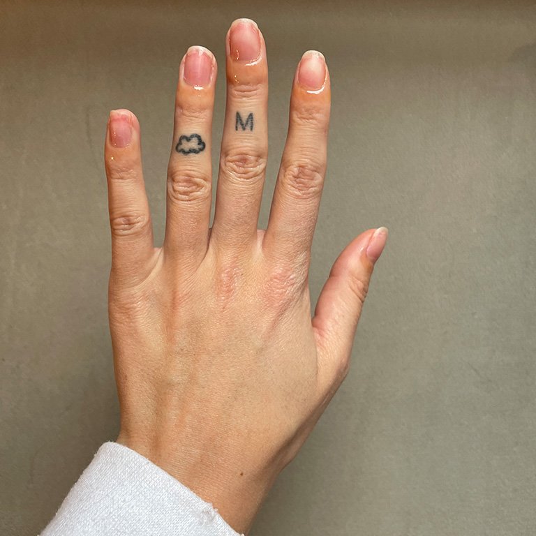 Editor's hand against a gray background with bare nails and cuticle oil