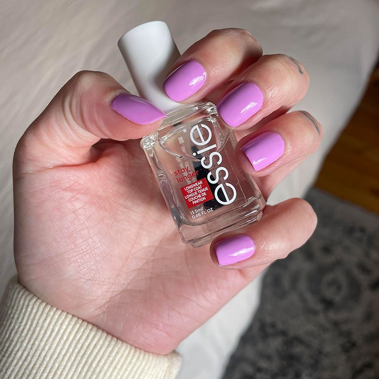 Photo of editor's hand with pink-purple nail polish holding the Essie Stay Longer Longwear Top Coat