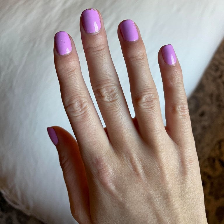 Photo of editor's hand with pink-purple nails with a small chip on the nail of the middle finger