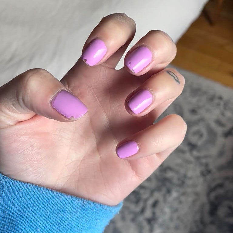 Photo of editor's hand with pink-purple nails and chips on some of the nails