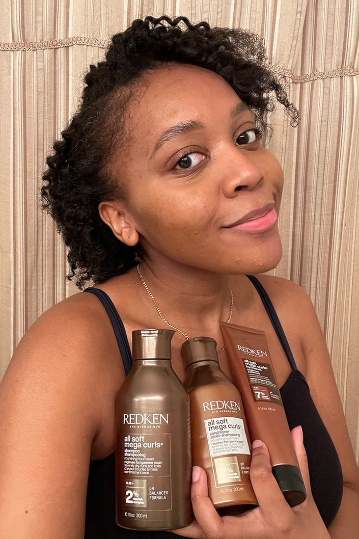 kat smiling holding the three redken soft curl line hair care bottles