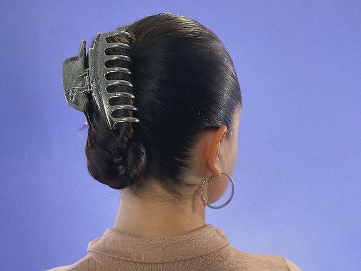 The back of someone's head with dark hair twisted up into a claw clip against a purple backdrop