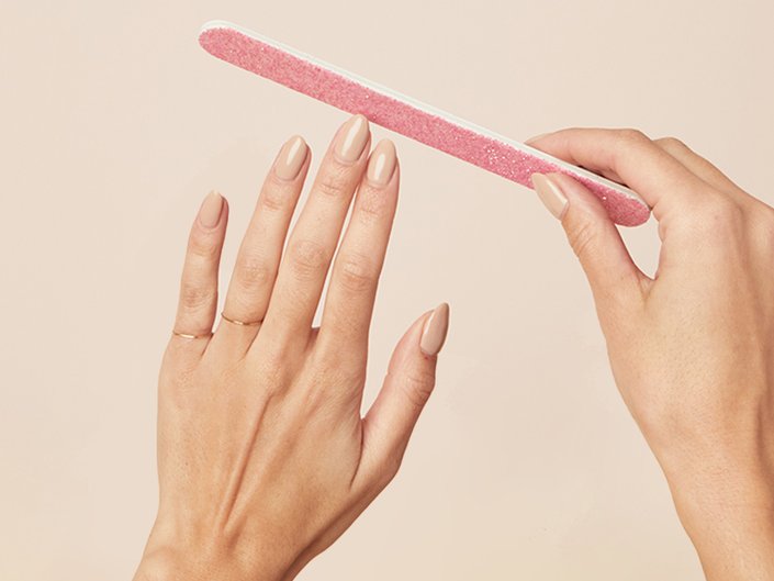 Picture of a person's hands with nude nail polish on, holding a pink nail file