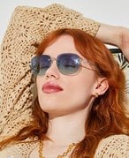 A person with red hair wearing blue sunglasses and a crocheted top lounges with their eyes closed on an orange floral beach chair