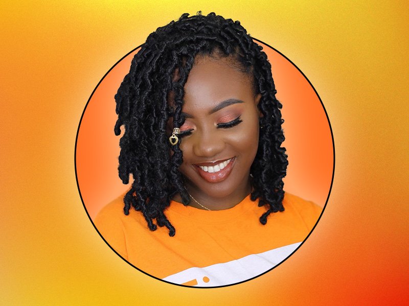 Person with orange makeup and butterfly locs smiling and looking down