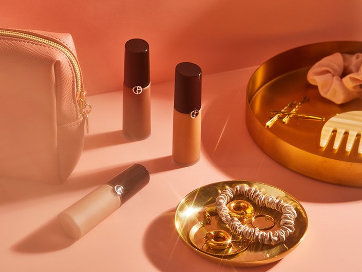 armani concealers photographed on a pink vanity set up with gold accessories, hair ties and a makeup bag