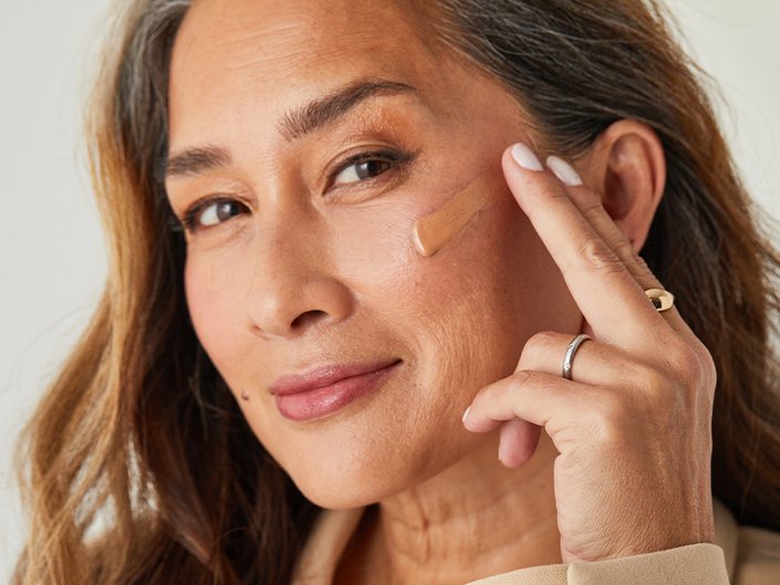 Person looking at the camera with tinted complexion makeup swatched on their cheek