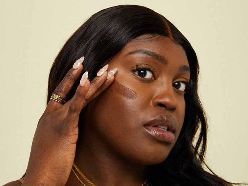 Close-up picture of a model applying foundation to the side of her cheek