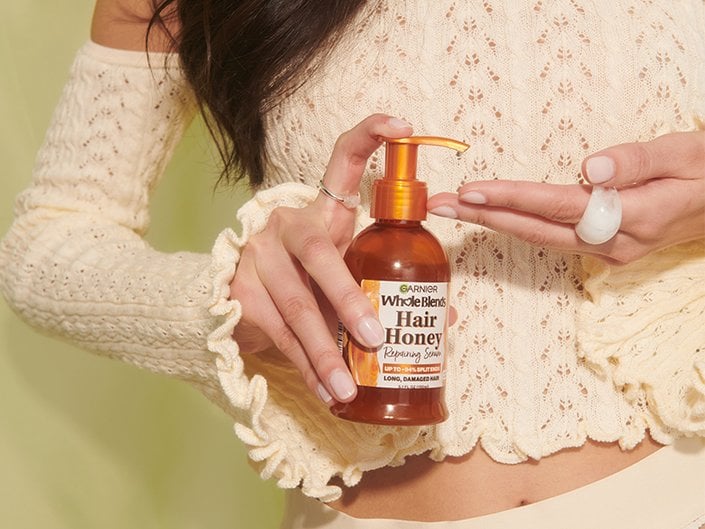 Close-up of a person’s hands pumping the Garnier Whole Blends Hair Honey Repairing Serum