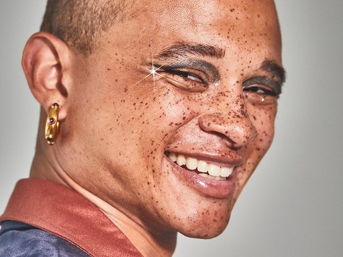 person with freckles smiling and wearing rhinestone eye makeup