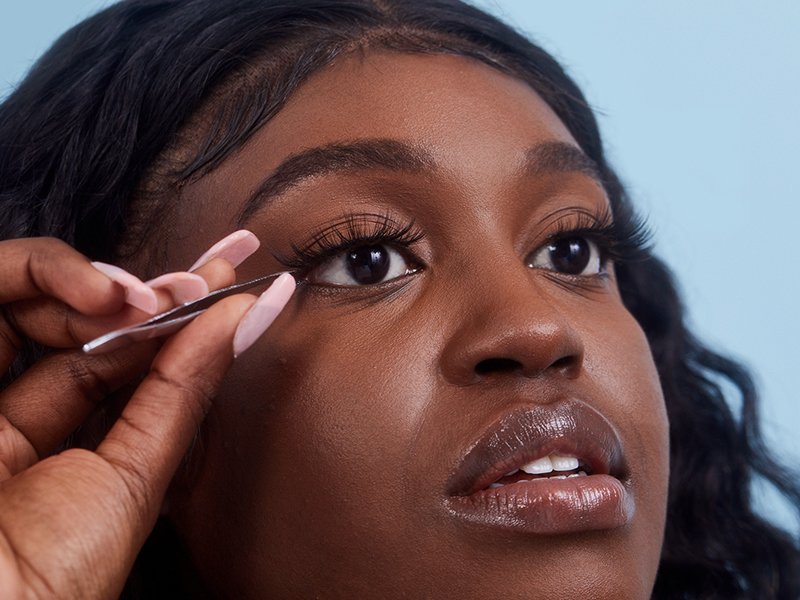Close up of a person applying false lashes with a tweezer