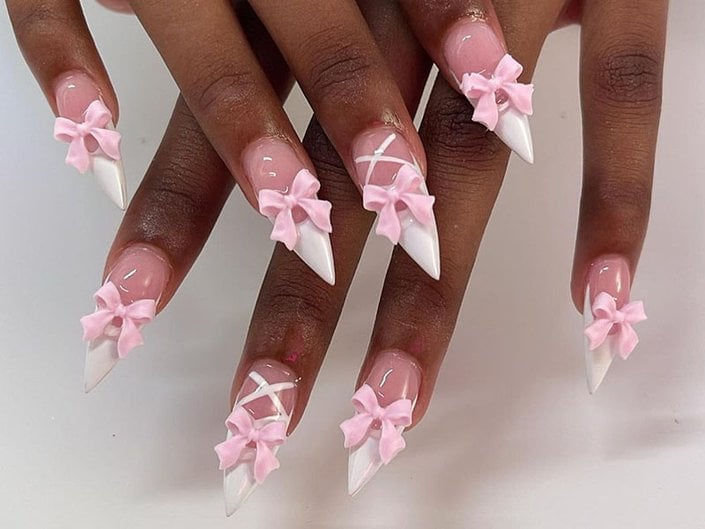 Close-up picture of a person's nails with pink bows and a white lace-up design