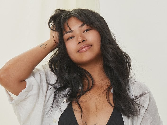 Person with long dark hair wearing a white shirt and holding one hand in their hair