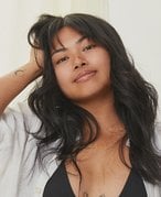 Person with long dark hair wearing a white shirt and holding one hand in their hair