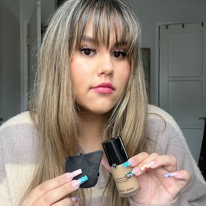Editor with long brown hair and bangs holding up Giorgio Armani Beauty Luminous Silk Foundation and powder puff