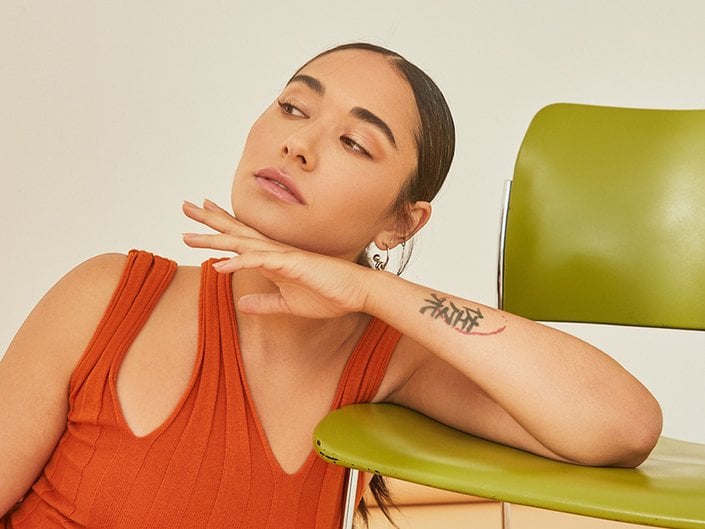 Picture of a model looking out of frame with their chin propped on their hand and their elbow resting on an olive green chair