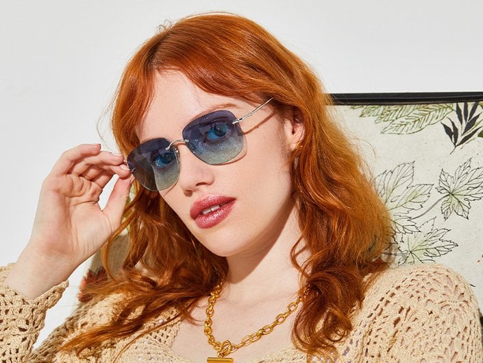 Picture of a model with red wavy hair wearing rectangular sunglasses with tinted blue lens.