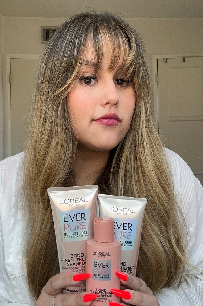 Editor with long brown hair and bangs holding up the L'Oréal EverPure Bond Strengthening System