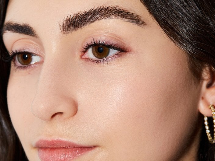 Close-up of a person’s face with long, dark hair, brown eyes and full eyebrows
