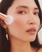 Close-up picture of a model holding a blush brush to their cheek