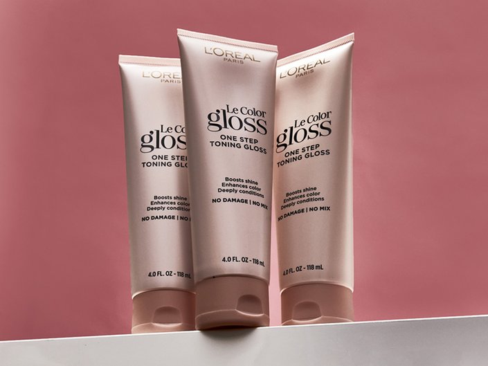 Three tubes of the L’Oréal Paris Le Color Gloss One Step In-Shower Toning Gloss against a red background
