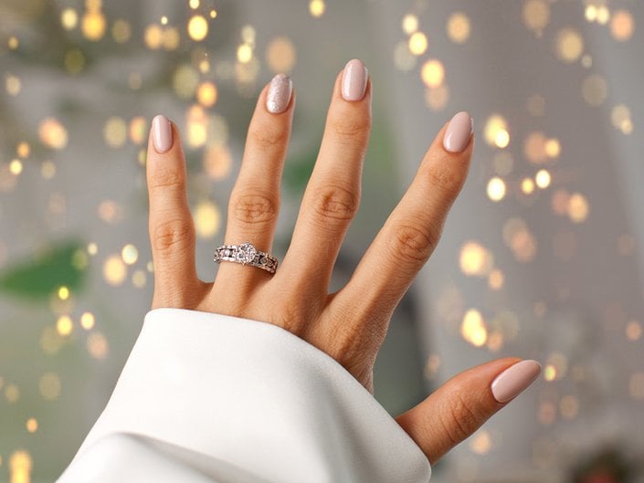 Hand with a diamond engagement ring and nails painted with light pink neutral nail polish