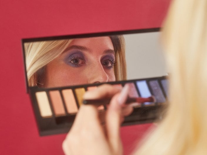 Person holding eyeshadow palette looking in the mirror