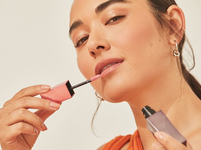 Person with dark hair applying lipstick to their lips