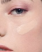 Swatches of different shades of liquid foundation on a green background.