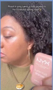 Woman showing the side of her face with glowing cheeks while holding a bottle of NYX Professional Buttermelt Bronzer