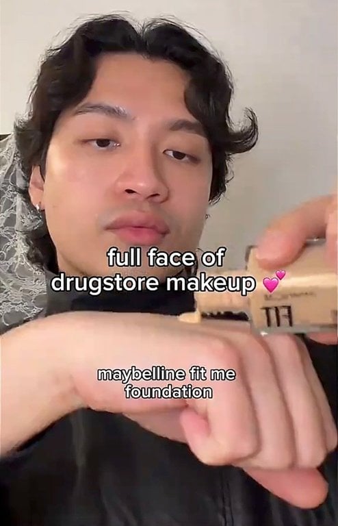 Person holding a bottle of Maybelline Fit Me Foundation next to their face before application.