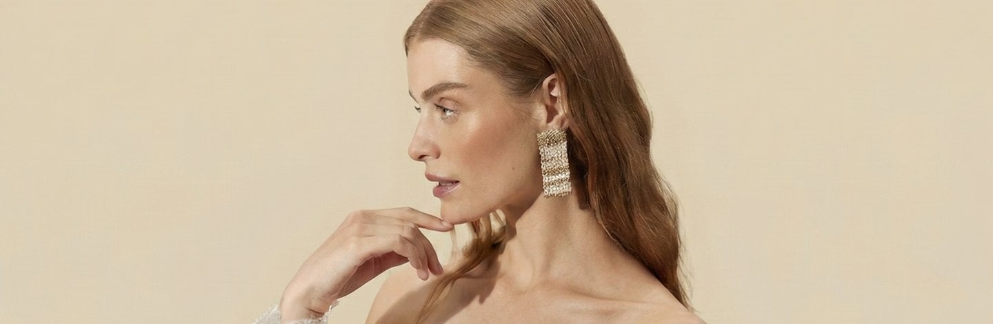 Woman’s side profile, wearing large gold earrings, an off the shoulder top, who has glowing skin