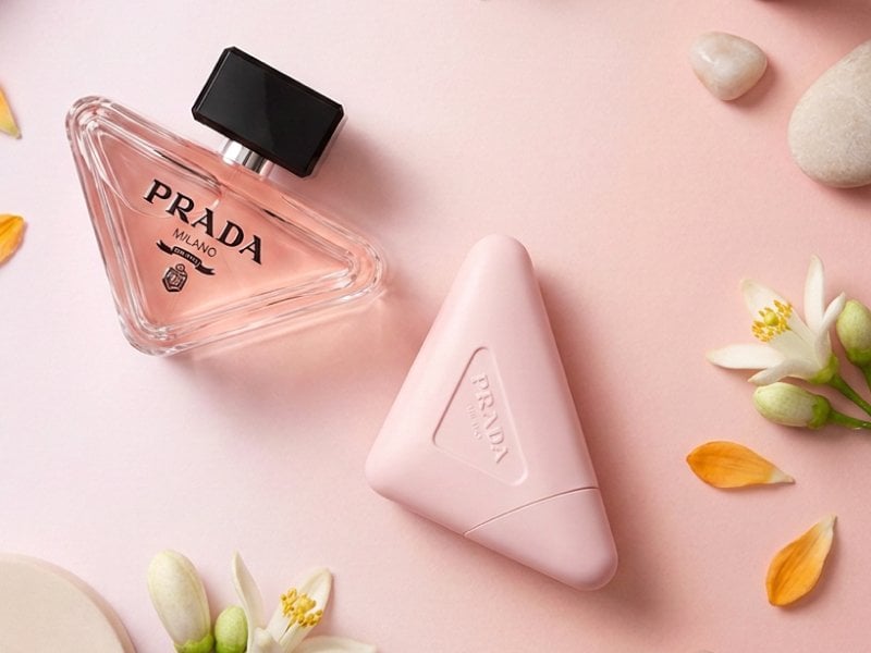 a visually appealing flat lay composition featuring a body lotion jar or tube and a perfume bottle on a soft neutral or brand-colored background, accented with floral elements or abstract props, but without any visible skin or human features.