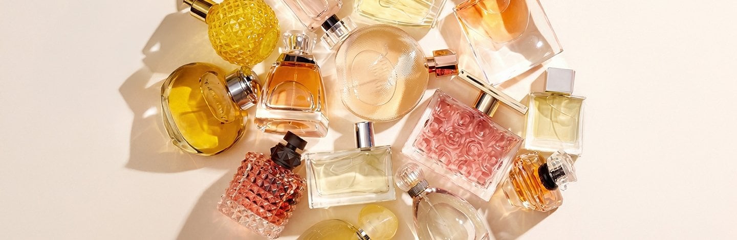 An image featuring a pile of unlabeled perfume bottles against a solid, light pink background.