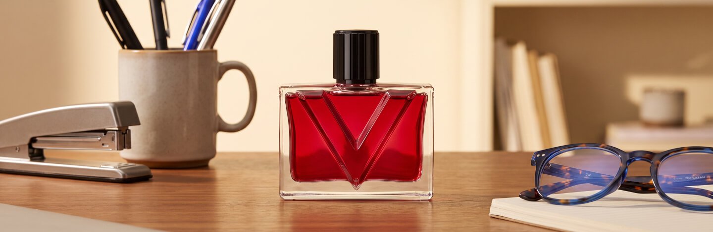 An office desk with a YSL perfume positioned on it along with various other desk accessories (staple, pens, laptop, blue light glasses, etc.)