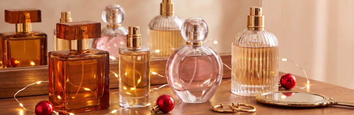 Perfume bottles wrapped in twinkly Christmas lights with some red ornaments laying nearby
